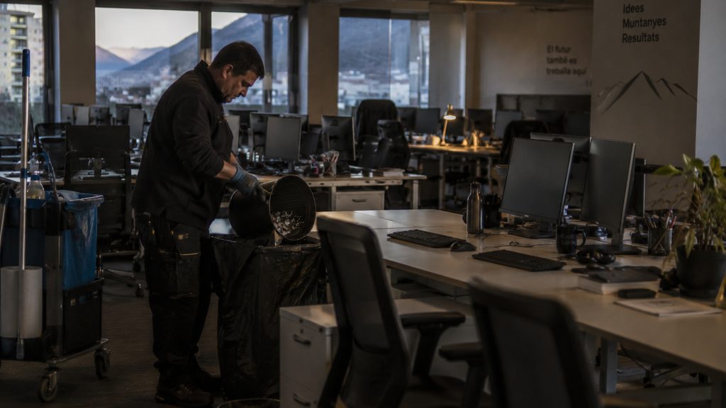 Operario vaciando las papeleras de una oficina diáfana de Andorra antes de que llegue la gente